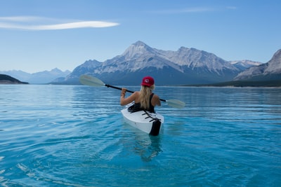 戴红帽的女子骑着白色皮划艇，面向阿尔卑斯山